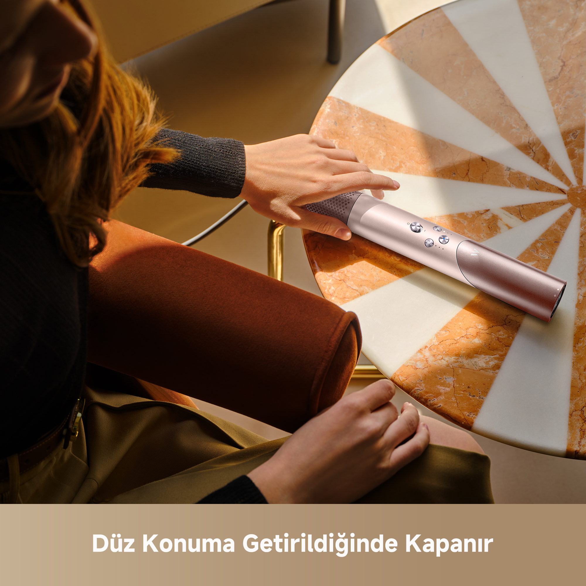 Bir kişi mermer masada gül altın rengi saç düzleştirici tutuyor.