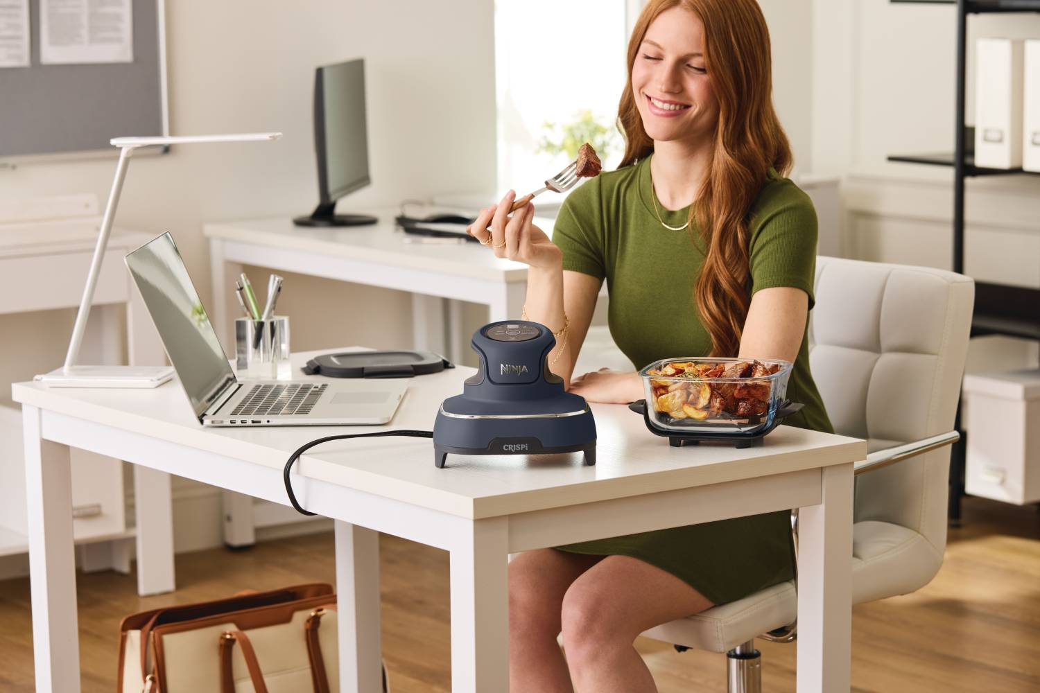 Mujer come carne de tenedor junto a Ninja Crisper. Entorno de oficina.