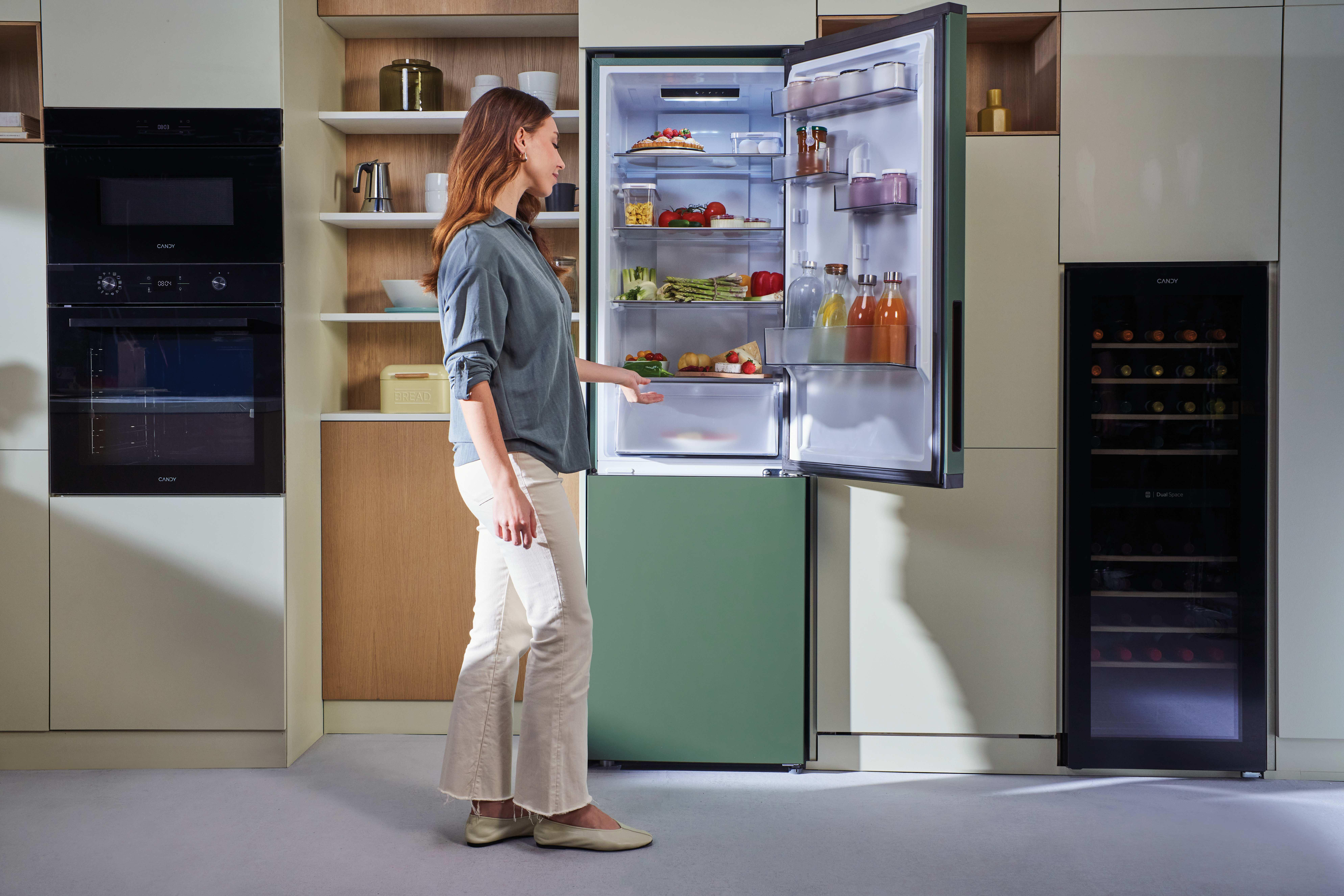 Eine Frau öffnet einen grünen Kühlschrank, daneben ein Weinregal.
