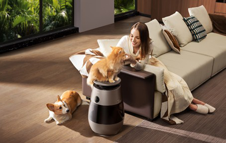Egy nő ül egy kanapén, miközben egy macska ül egy légtisztítón, és egy corgi fekszik mellette.