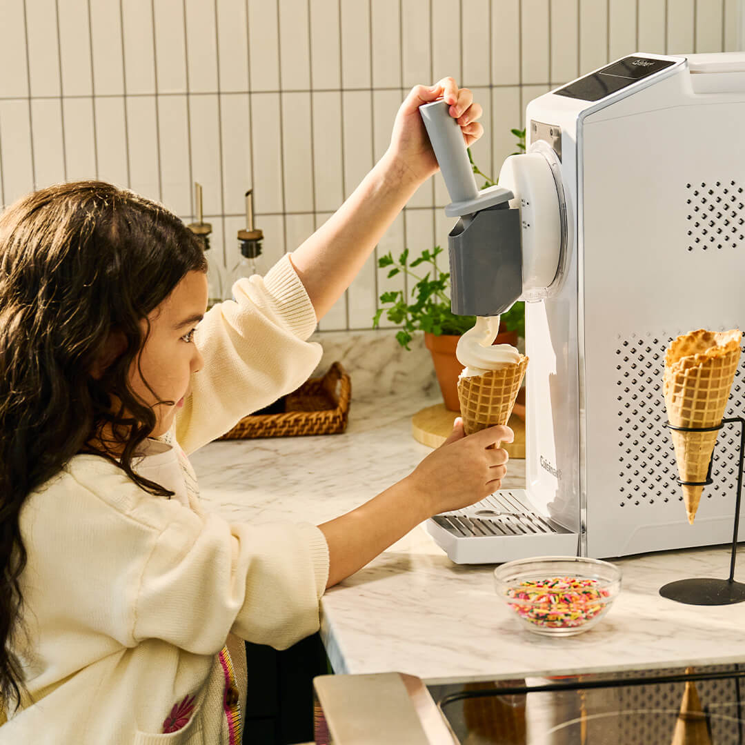 Ein Mädchen macht Eiscreme in einem Waffelhorn mit einer Eismaschine.