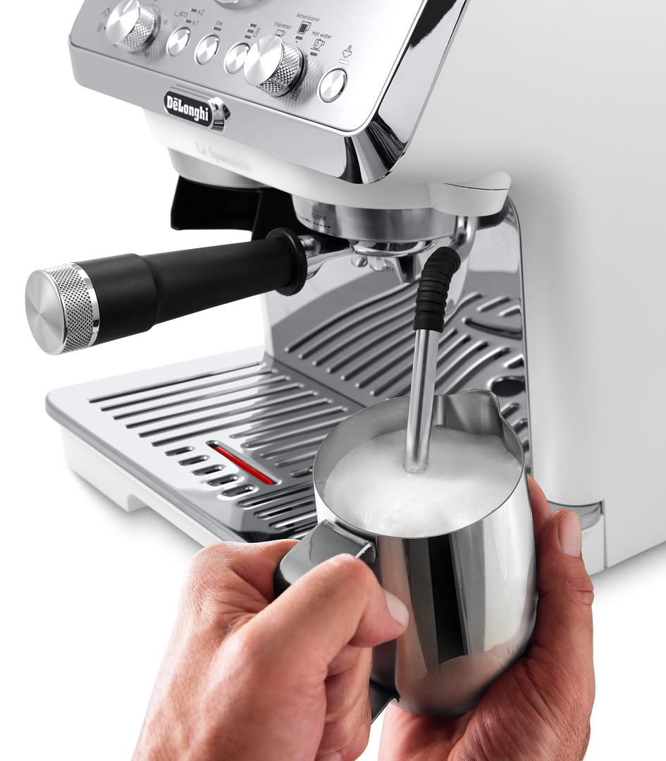 Hände schäumen Milch in einer Kanne mit einer Kaffeemaschine.