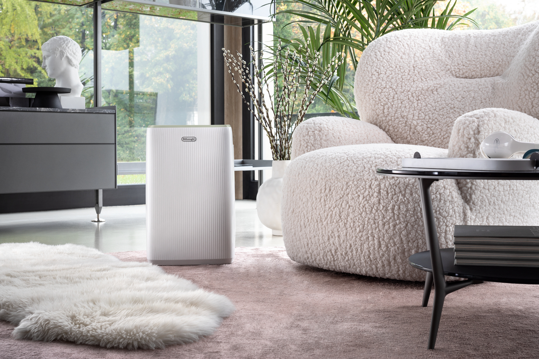 Ein weißer Luftreiniger steht neben einem flauschigen Sessel in einem modernen Wohnzimmer.
