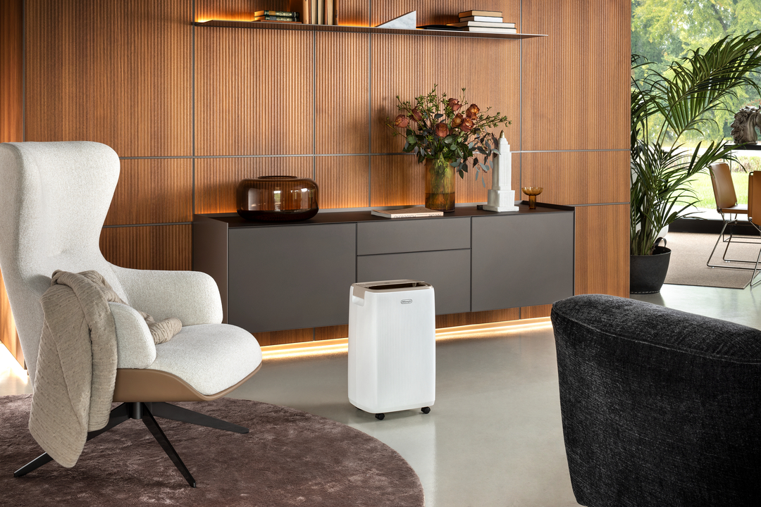 Ein weißer Luftkühler steht vor einem dunklen Sideboard mit Holzverkleidung.