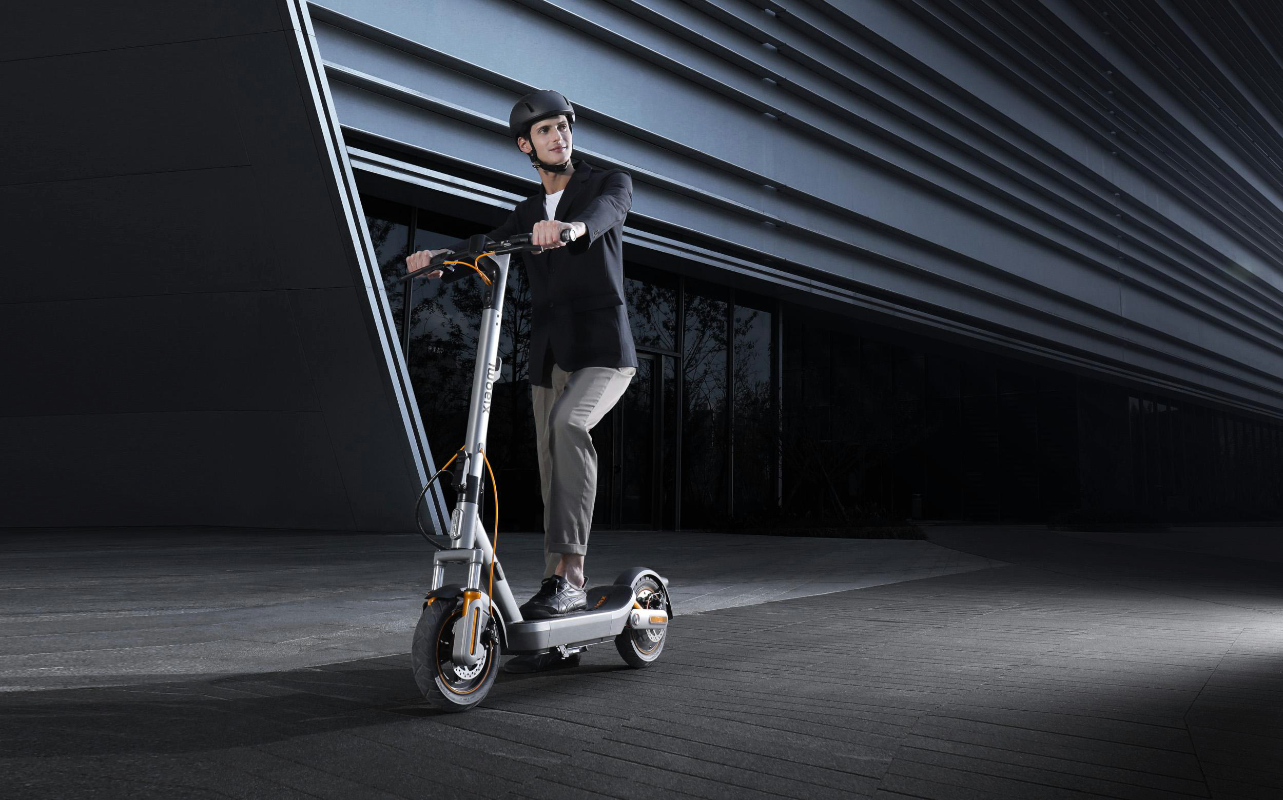 Mann mit Helm fährt E-Scooter vor modernem Gebäude
