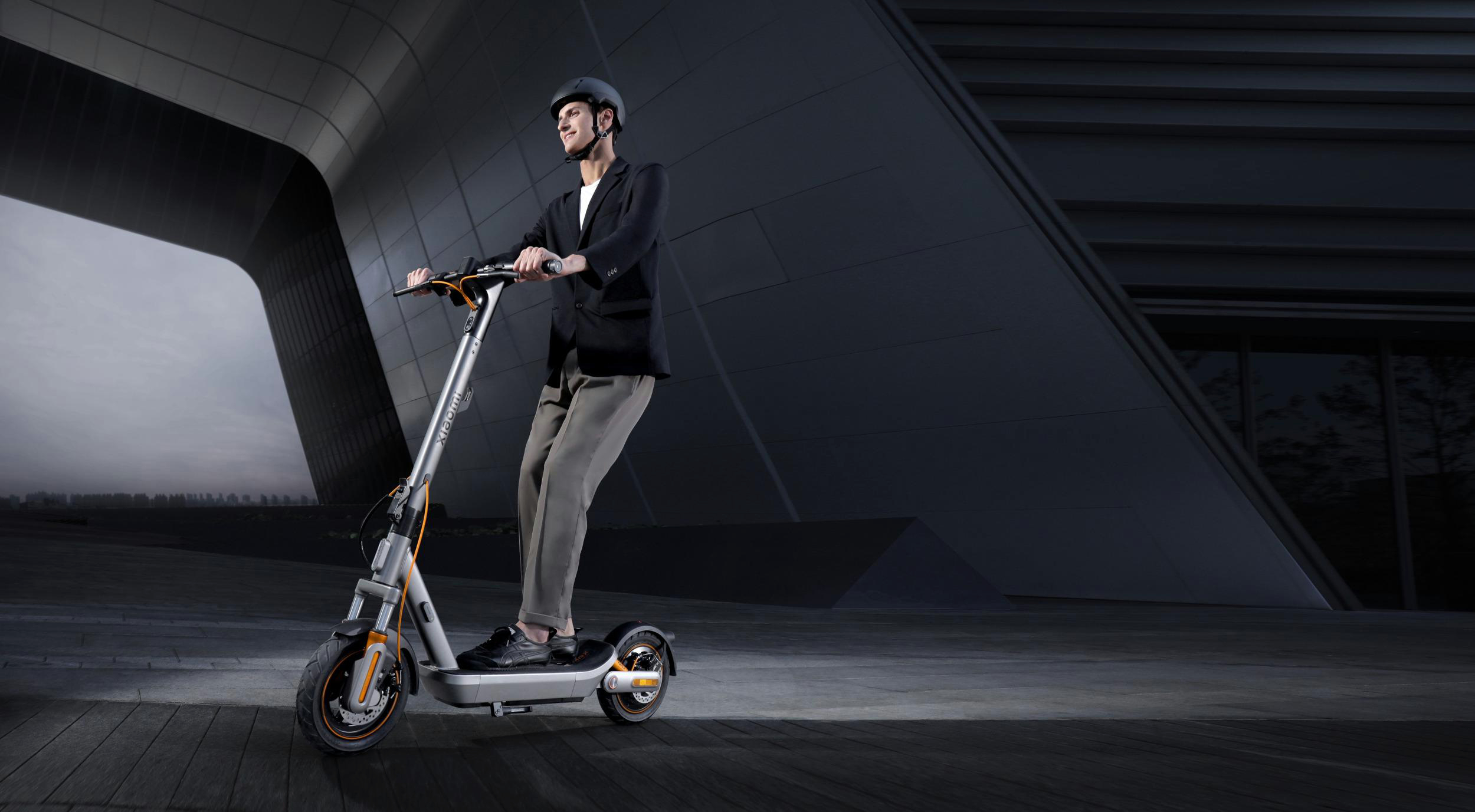 Ein Mann mit Helm fährt auf einem E-Scooter vor einem modernen Gebäude.