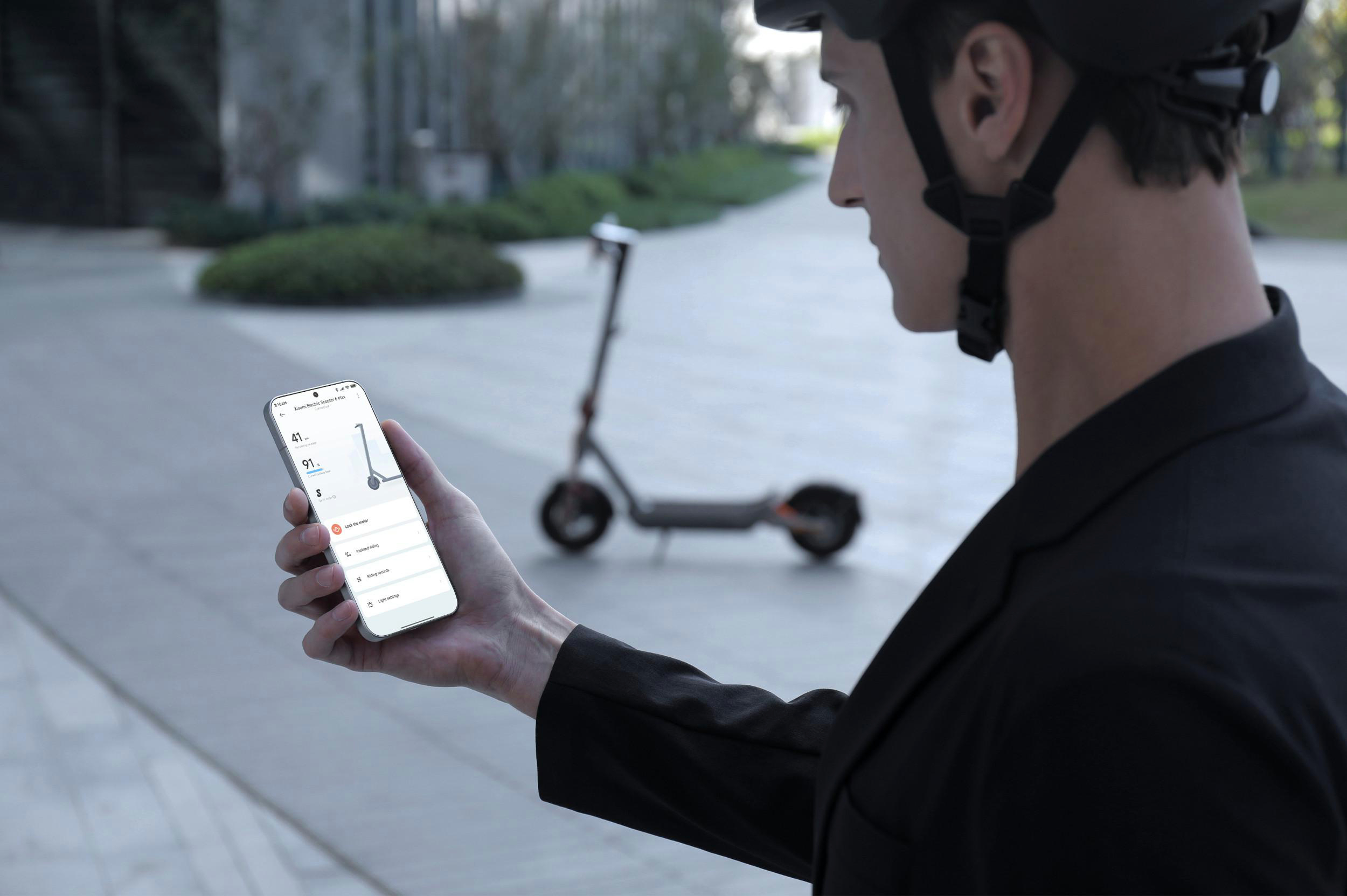 Mann mit Helm benutzt Handy mit E-Scooter-App, E-Scooter im Hintergrund.