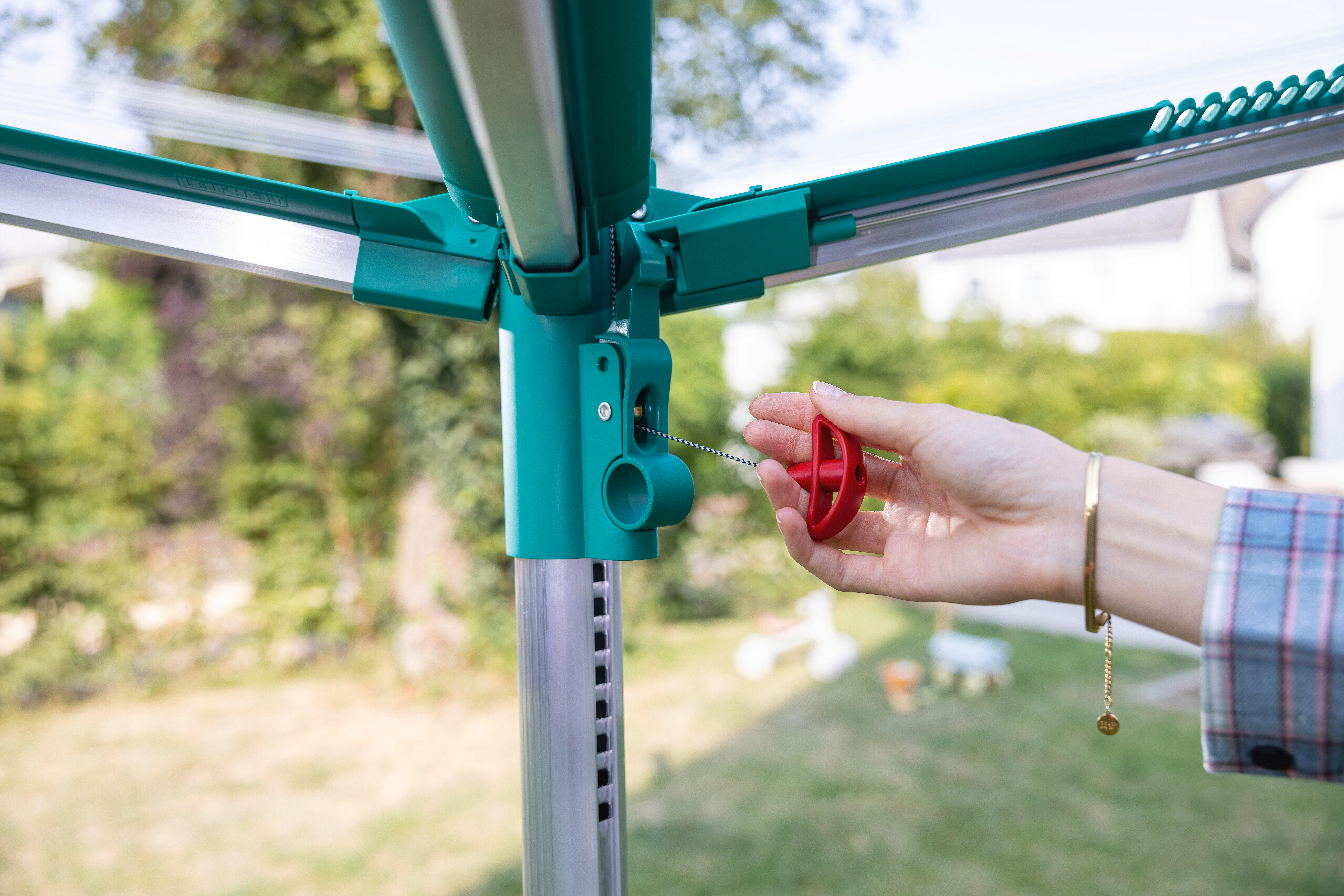 Hand dreht roten Griff eines grünen Wäscheständers im Garten.