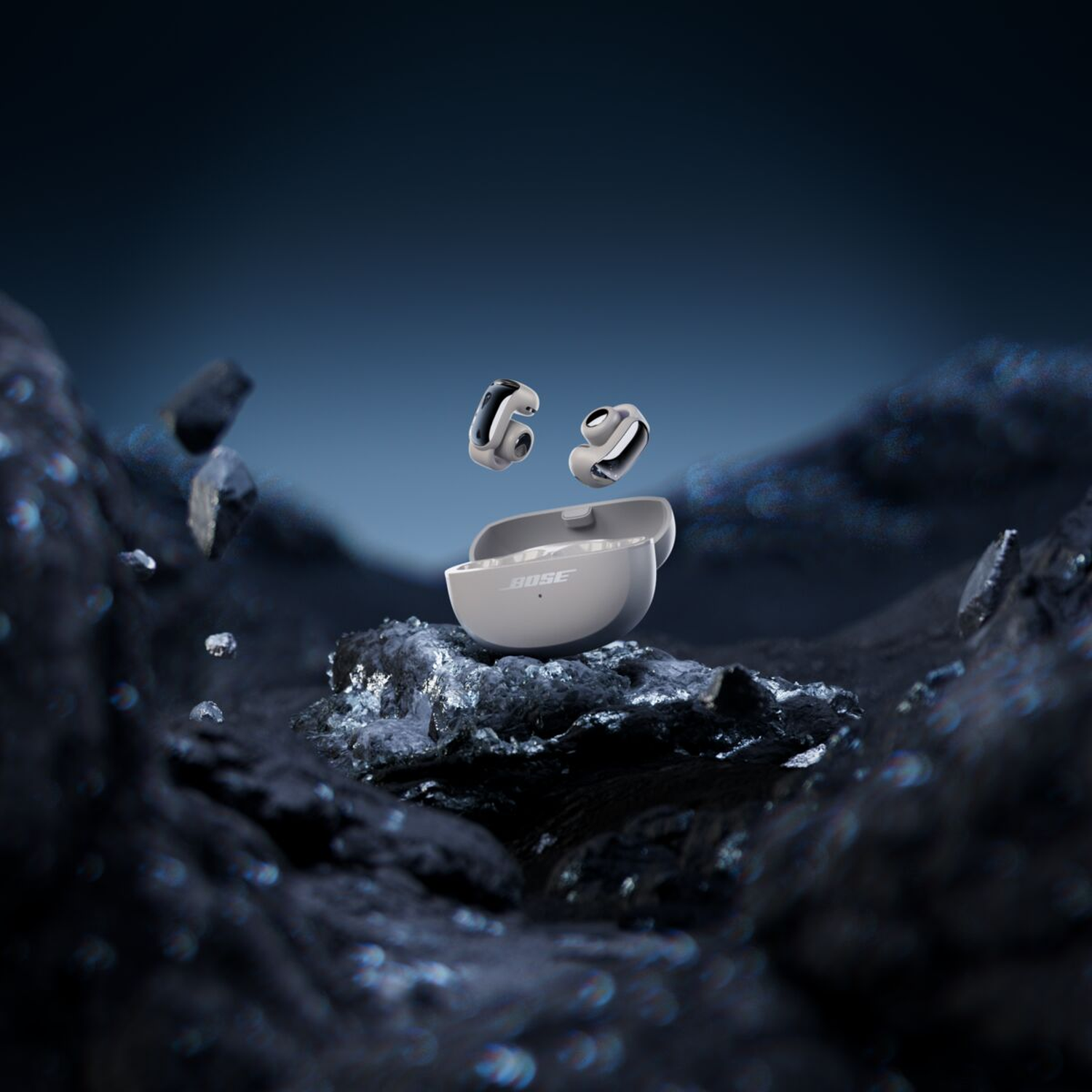 White Bose earbuds hover above an open charging case on dark rocks.