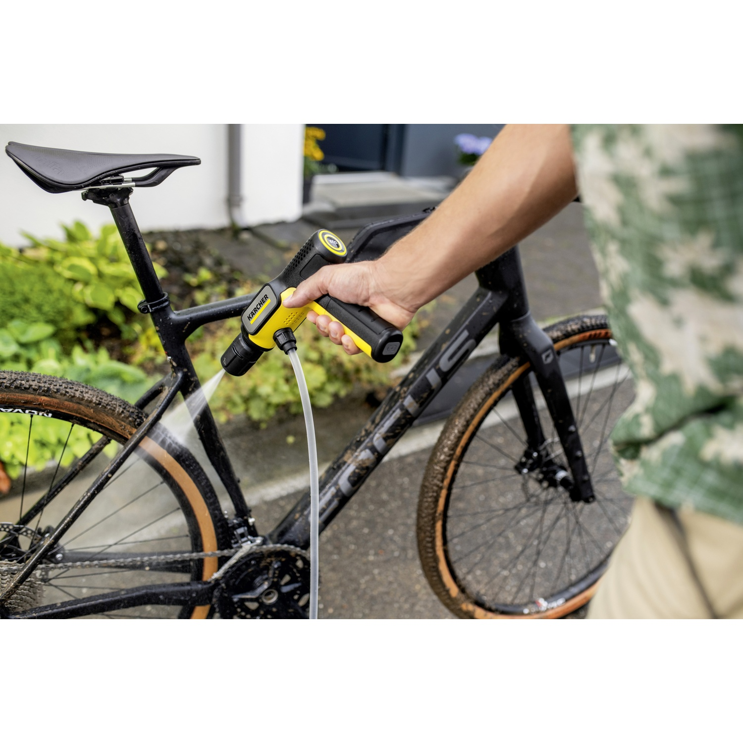 A hand cleans a dirty bicycle with a yellow Kärcher cleaner.