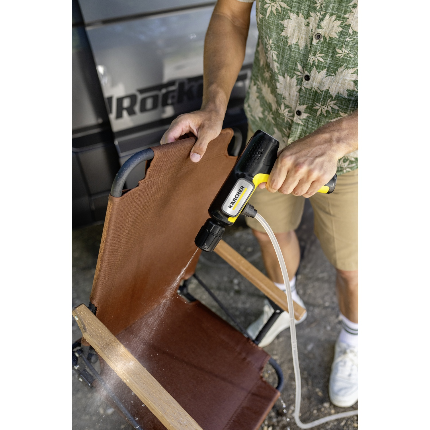 Man cleans brown chair with Karcher cleaner. Water sprays.