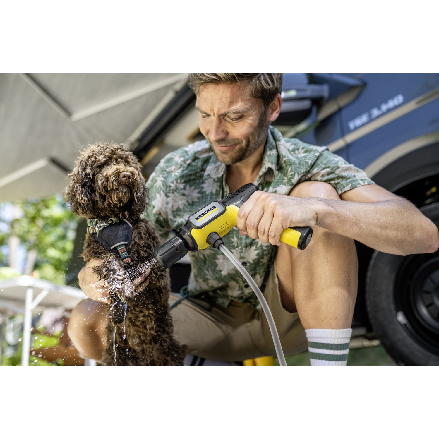Man washes dog with Kärcher cleaner outdoors.