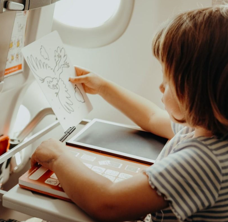 Kind malt einen Vogel im Flugzeug. Serviertablett hält Tablet und Zeichenbuch.