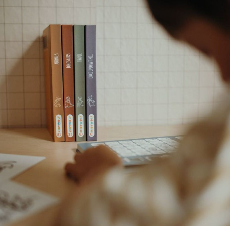 Vier Bücher stehen auf einem Schreibtisch, daneben eine Tastatur. Ein Kind tippt.