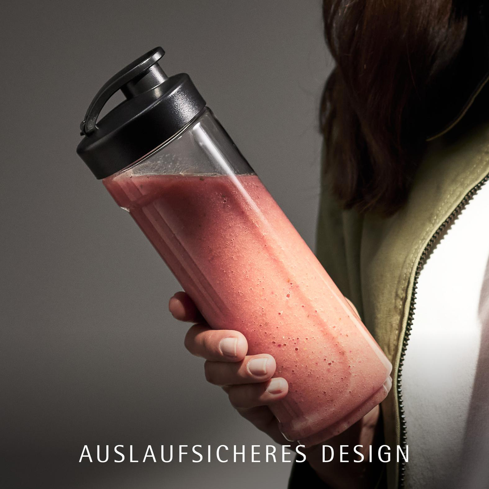 Eine Hand hält eine durchsichtige Flasche mit rosafarbenem Smoothie und schwarzem Deckel.