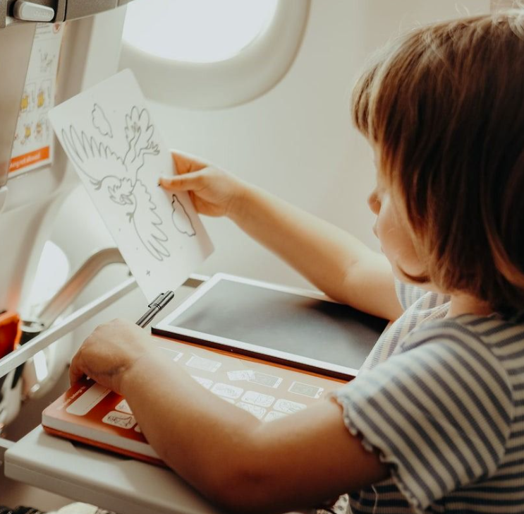 Kind zeichnet im Flugzeug mit einem Stift neben einem Tablet.