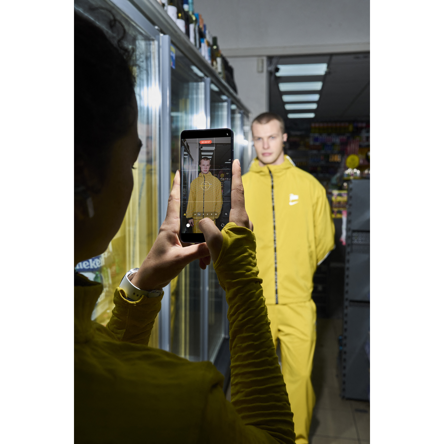 Person photographs a man in a yellow suit inside a supermarket.