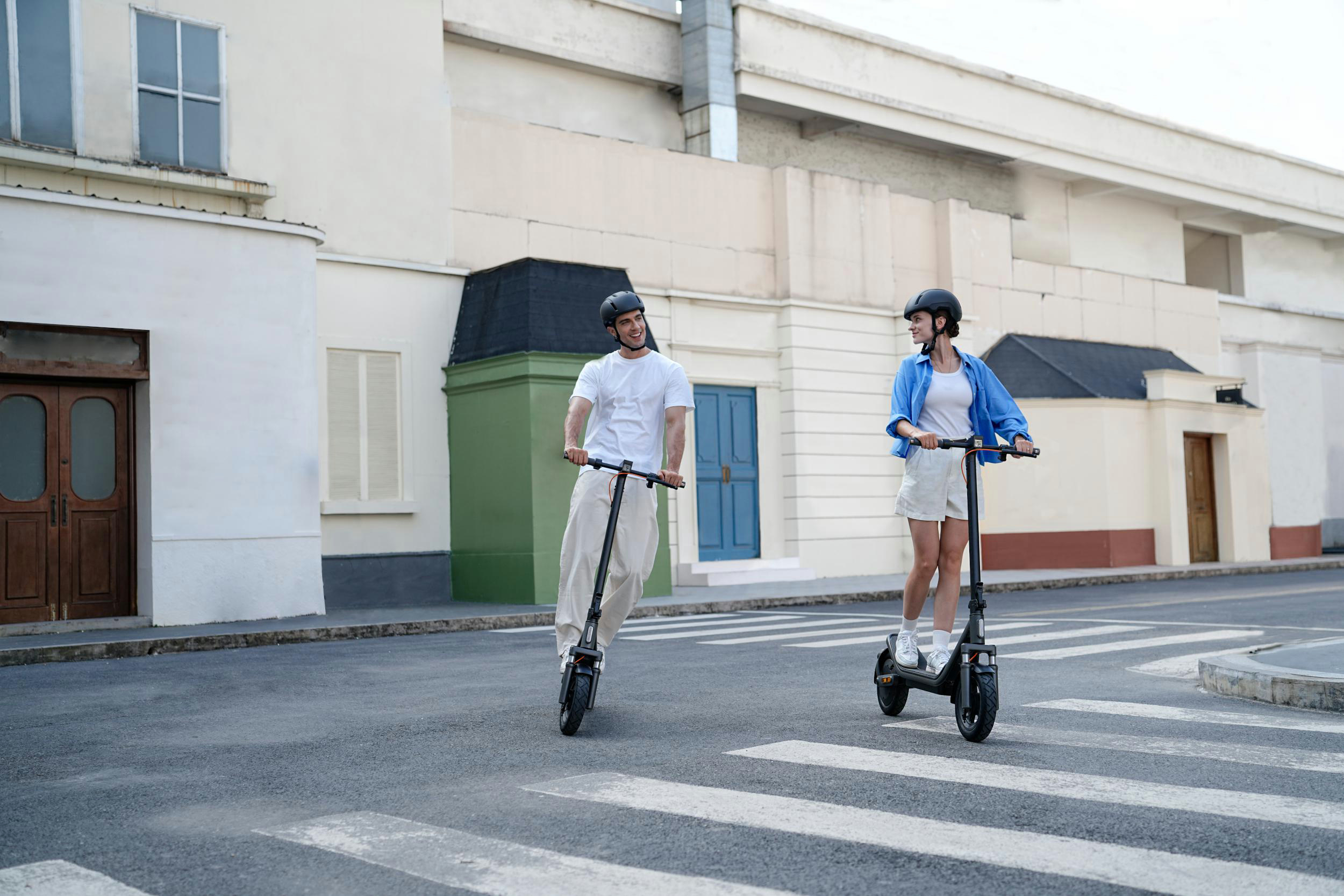 Mann und Frau fahren E-Scooter in der Stadt, tragen Helme.