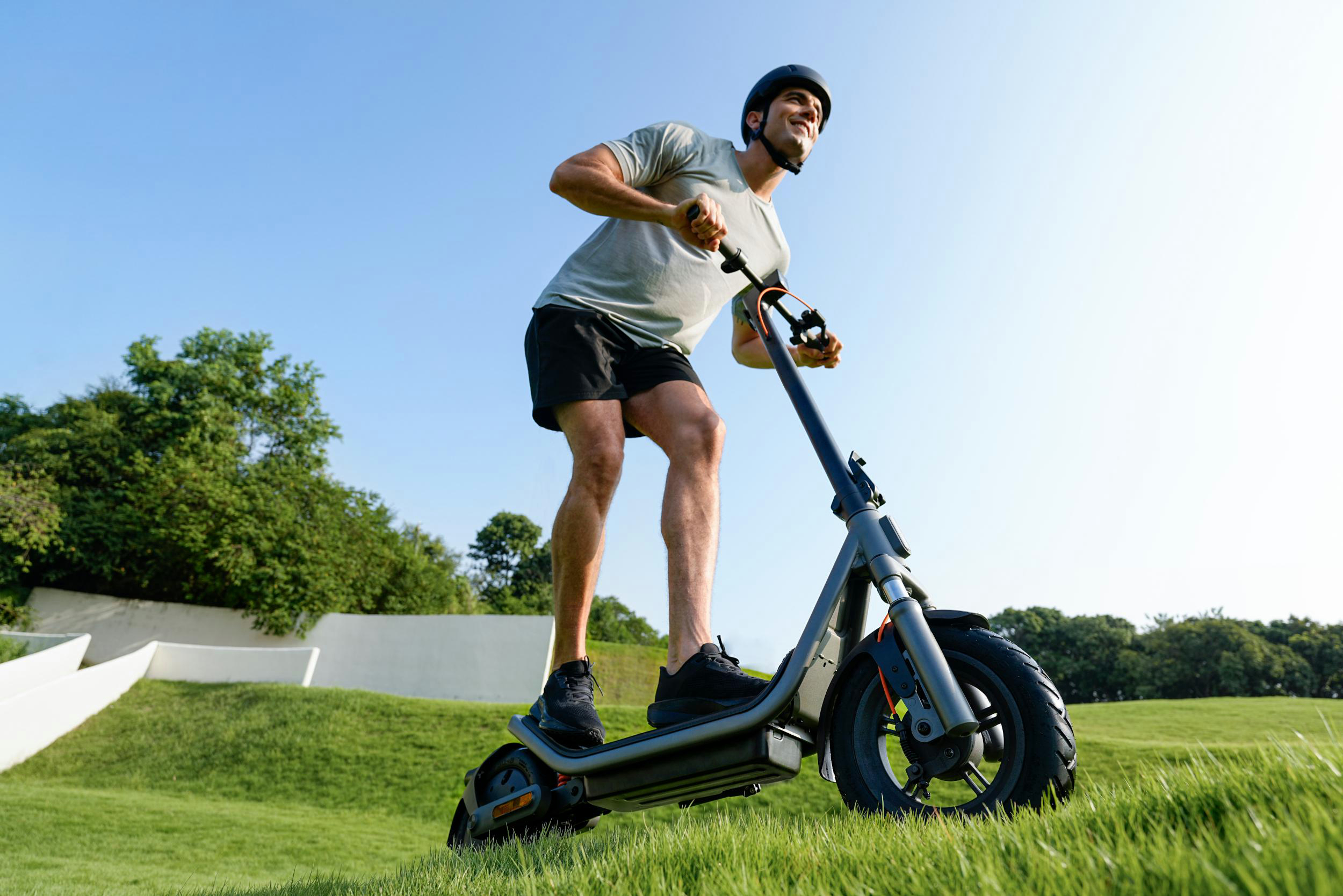 Mann fährt E-Scooter im Park auf grünem Rasen unter blauem Himmel.