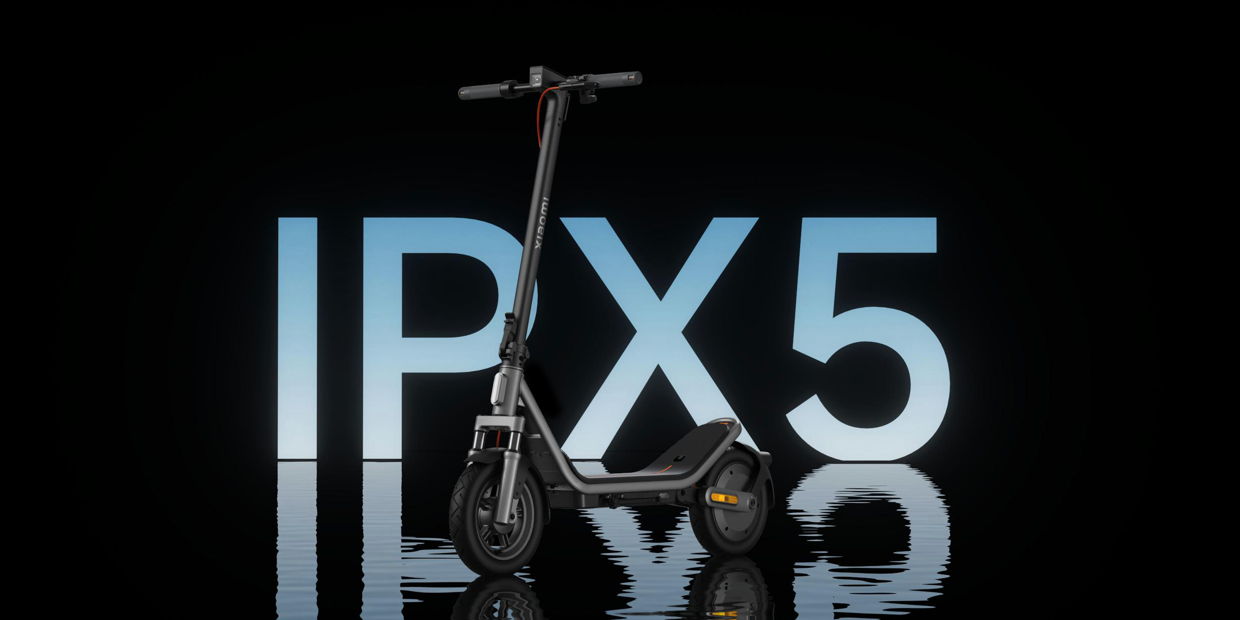 Ein grauer Xiaomi E-Scooter steht auf spiegelndem Wasser vor großen blauen IPX5-Buchstaben.