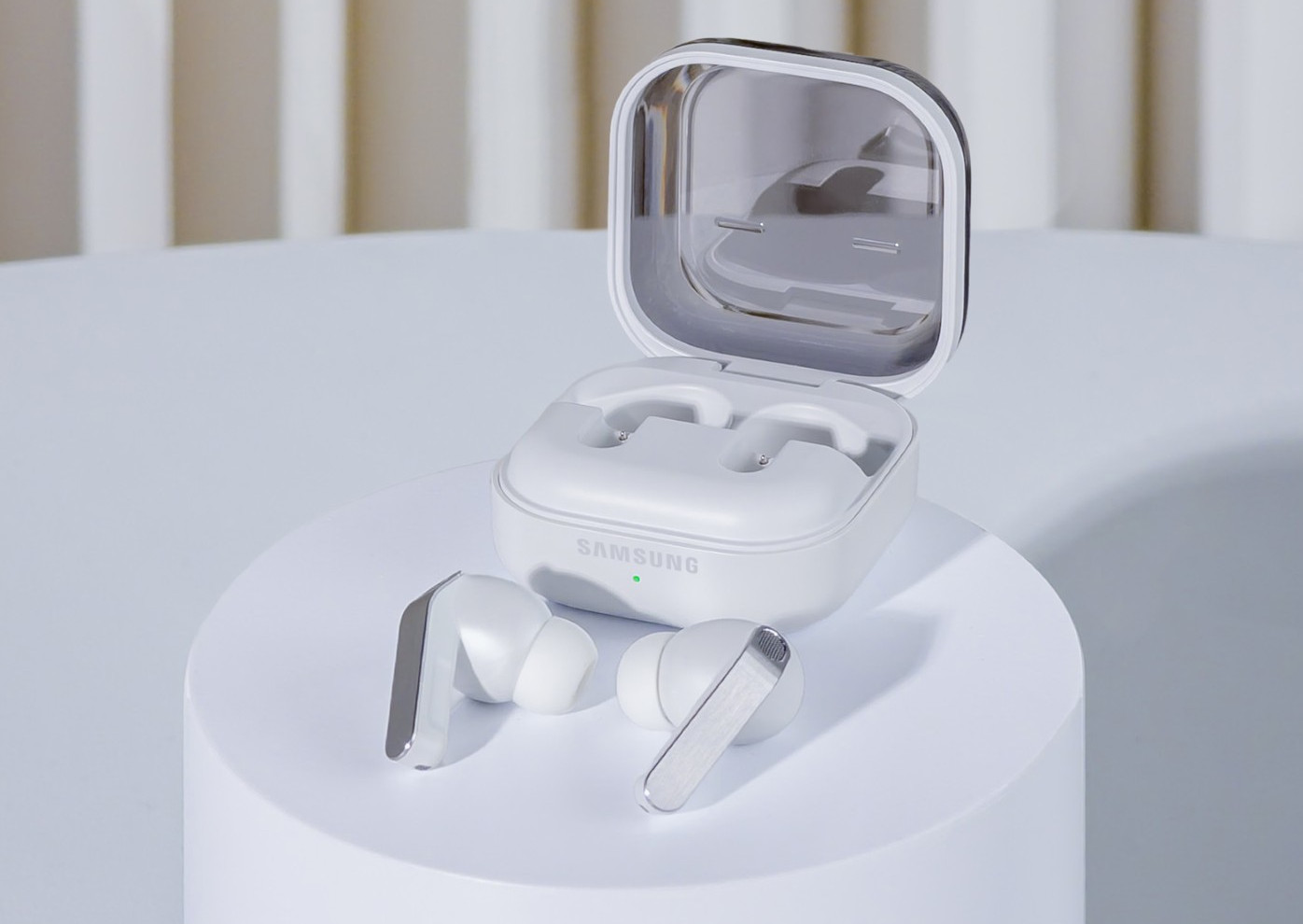 Białe słuchawki Samsung z etui ładującym na postumencie.