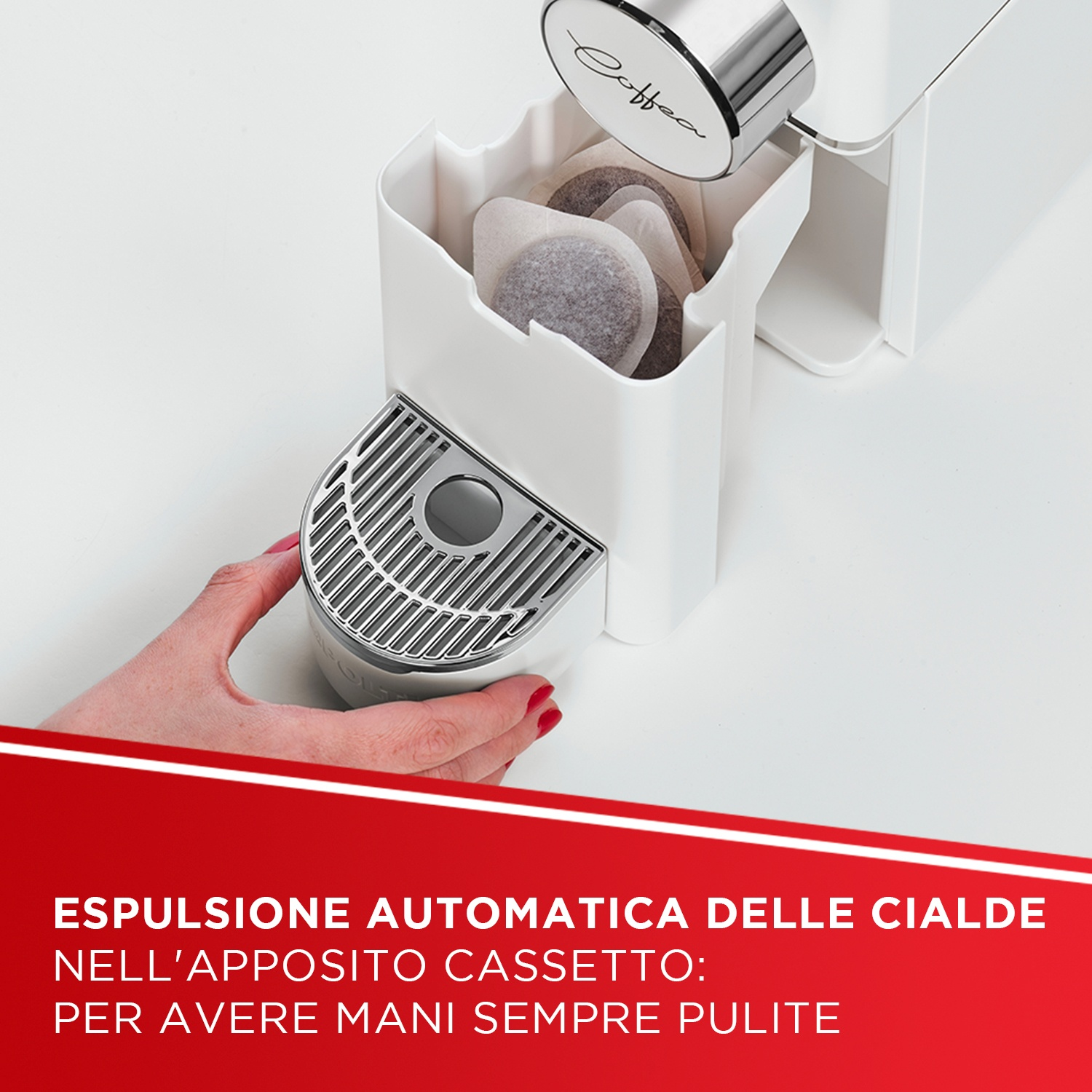 Una mano aziona una macchina da caffè bianca che espelle le capsule in un cassetto.
