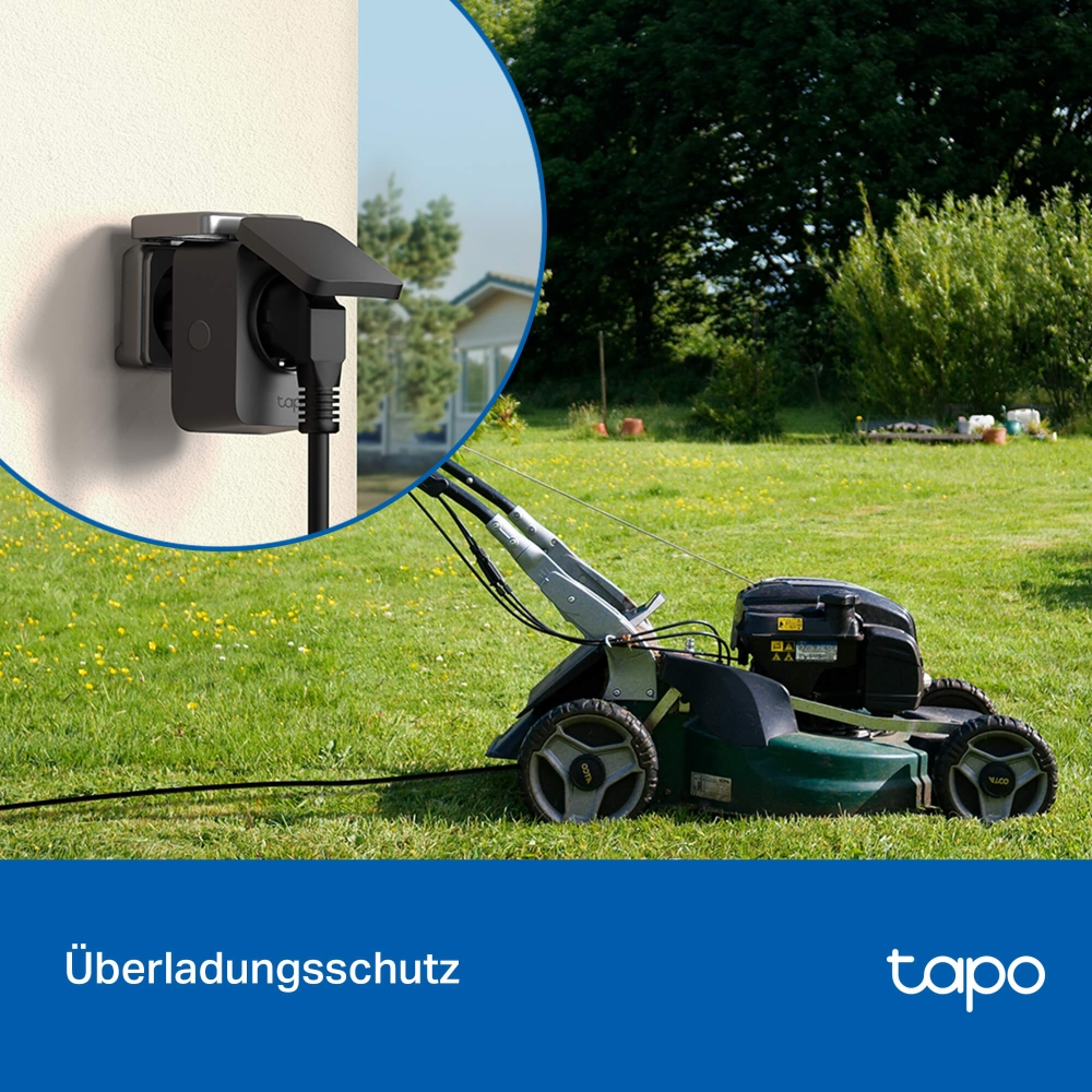 Ein Rasenmäher steht im Gras. Eine Steckdose ist an der Wand.
