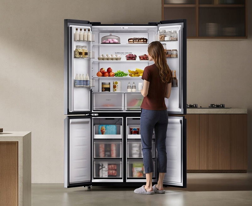 Kobieta stoi przed otwartą lodówką wypełnioną jedzeniem.