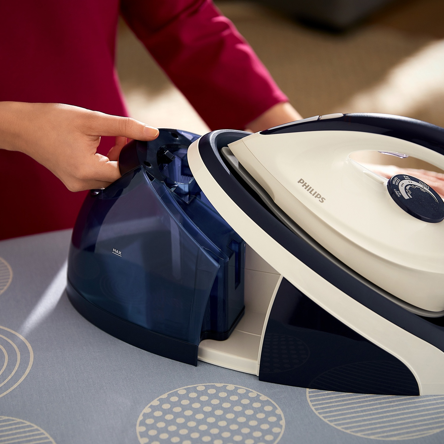 A hand operates a steam iron's water tank on an ironing board.