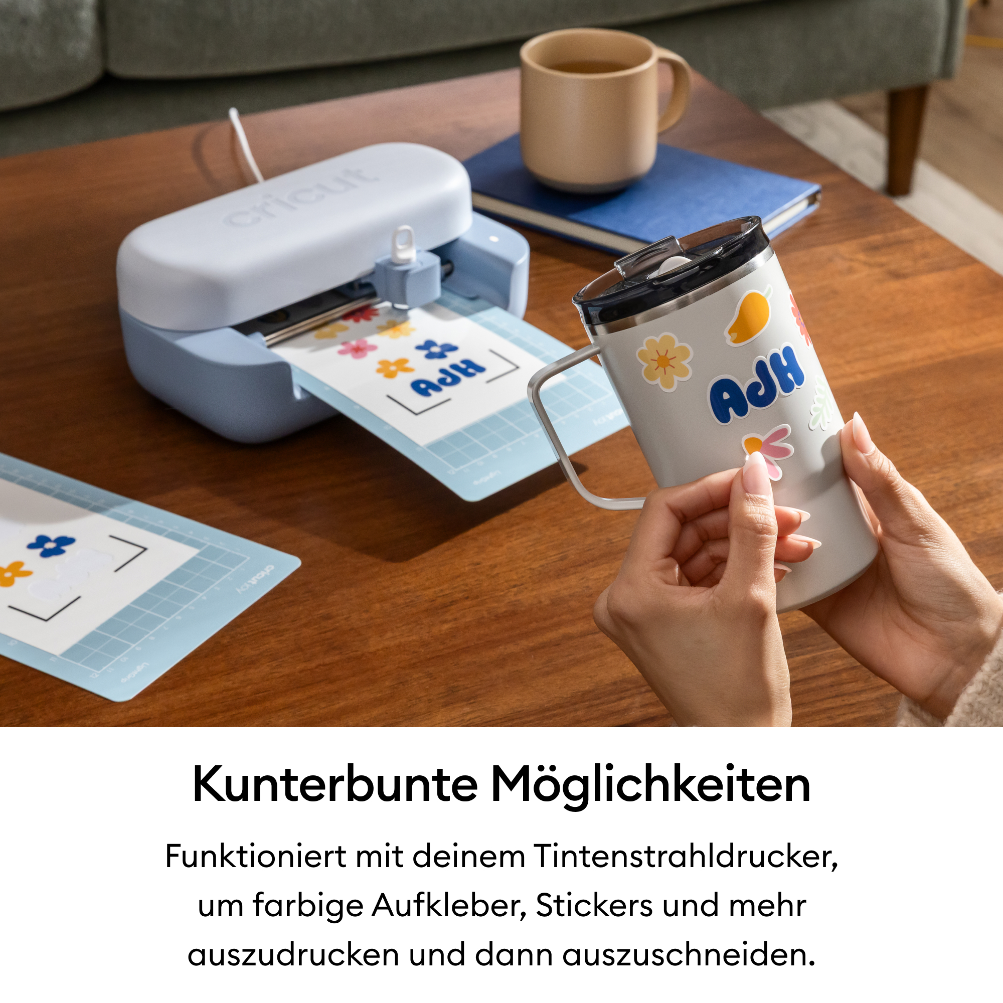 Eine Person dekoriert eine Tasse mit bunten Stickern, während ein Schneidegerät daneben liegt.