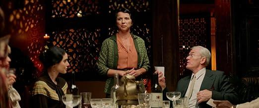 Eine Frau steht am Tisch, während Männer und Frauen sitzen. Sie ist im Fokus.