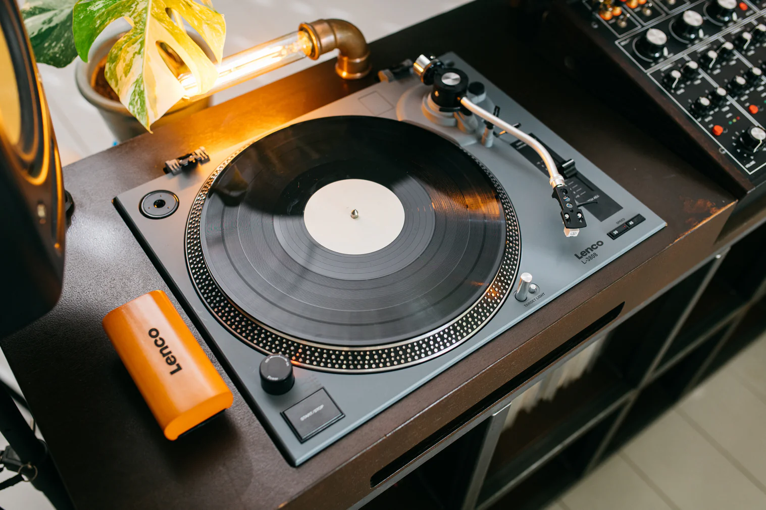 Ein Plattenspieler mit Vinyl, orangefarbener Kappe, Lampe und Pflanze.