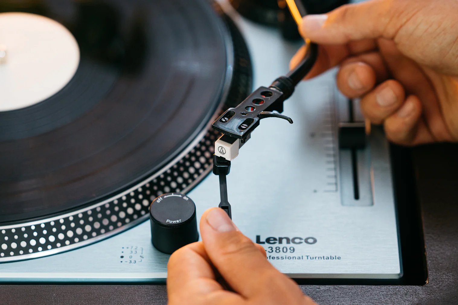 Hände bedienen einen Lenco Plattenspieler mit einer Vinylplatte.