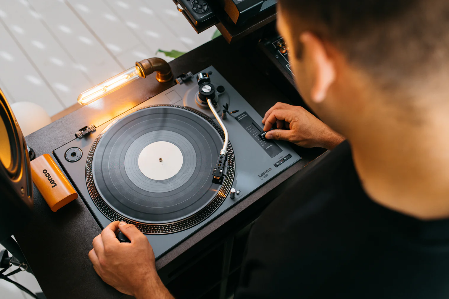 Mann bedient einen Plattenspieler mit Vinyl-Schallplatte und Glühbirnenlampe.