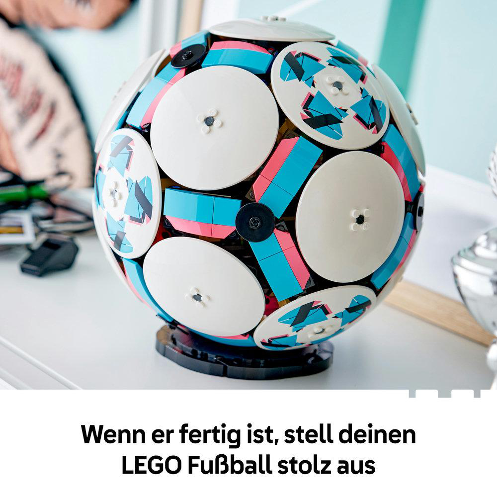 Ein bunter Lego-Fußball steht auf einem Sockel, mit Teilen in Weiß, Blau und Rosa.