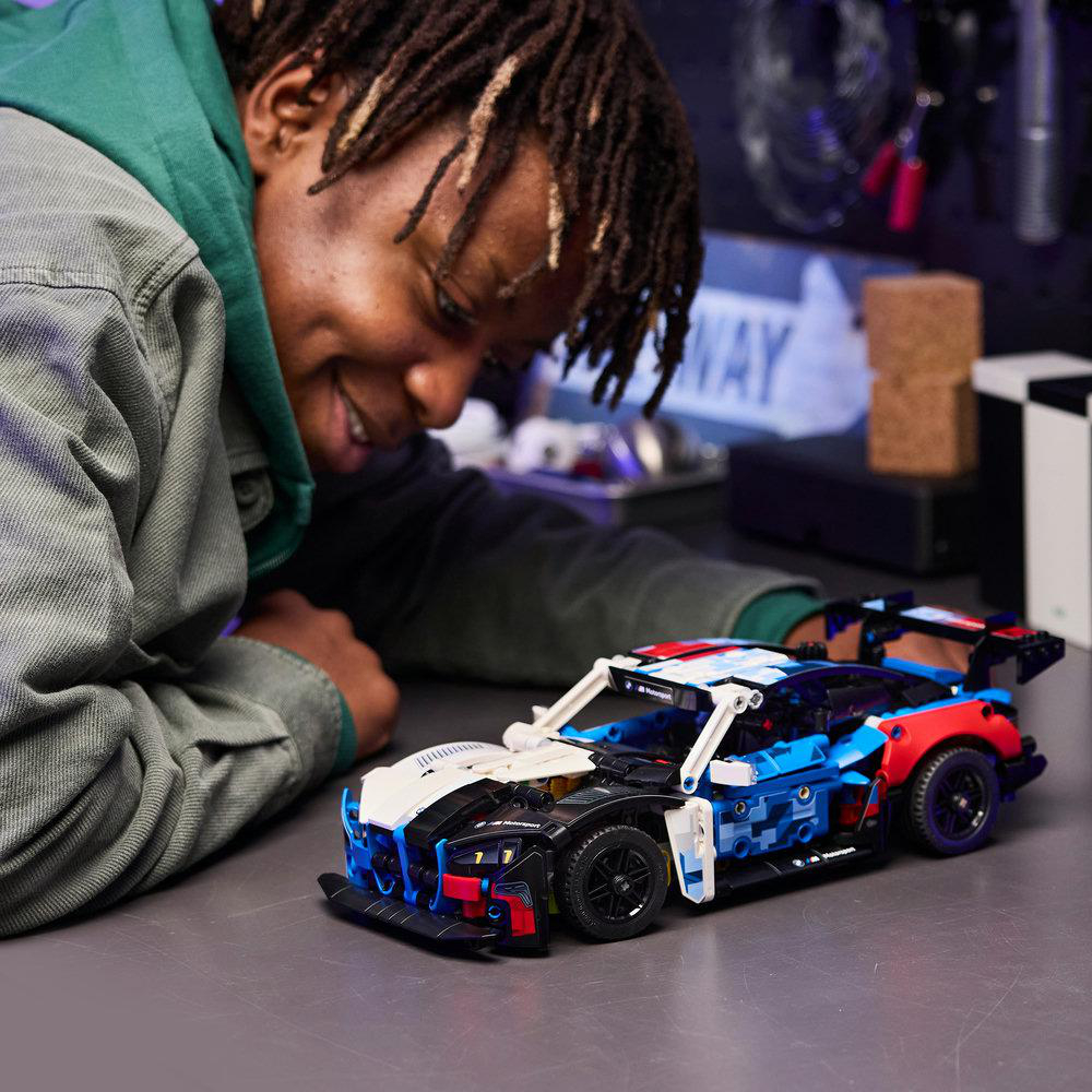 Ein Mann blickt auf ein detailliertes Lego-Auto in den Farben Blau, Rot und Weiß.