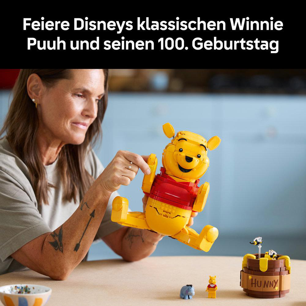 Frau hält eine LEGO Winnie Puuh Figur. Daneben stehen kleine Figuren und ein Honigtopf.
