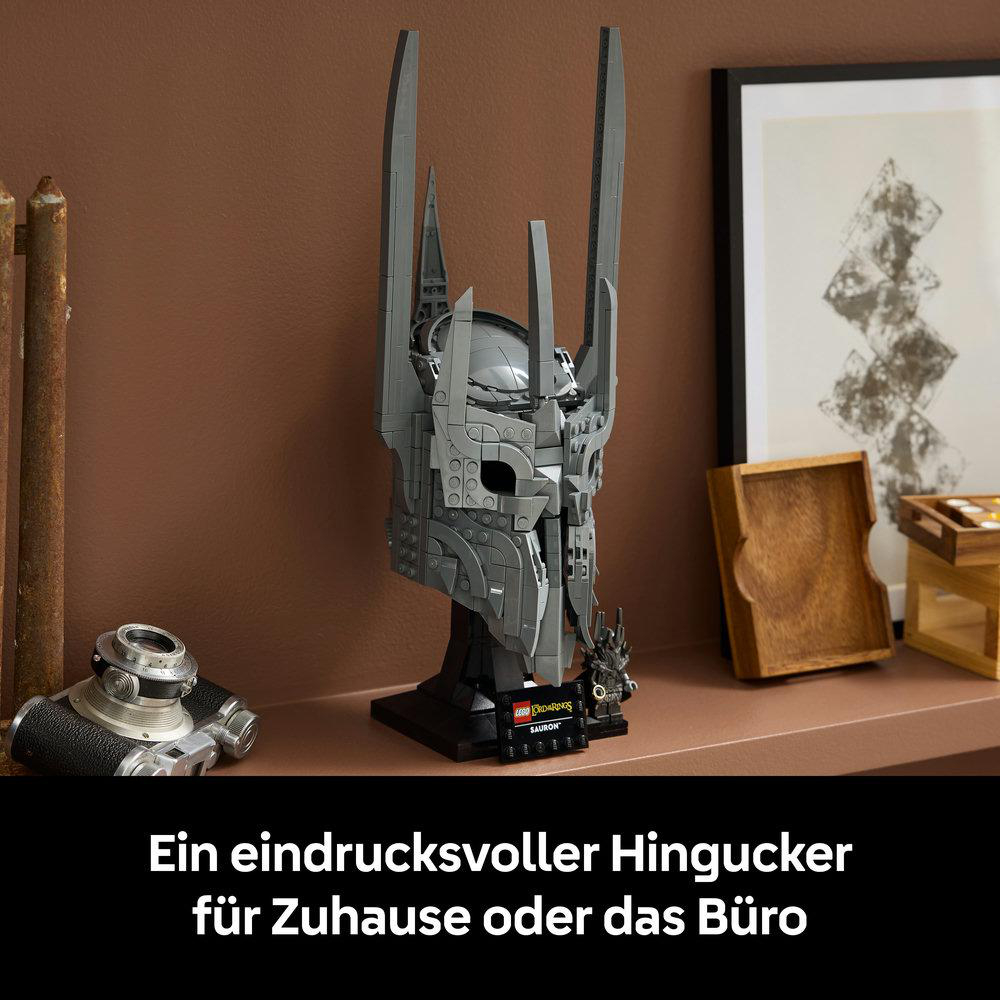 Grauer Helm von Sauron aus Lego auf einem Ständer, daneben eine Kamera und Bilder.