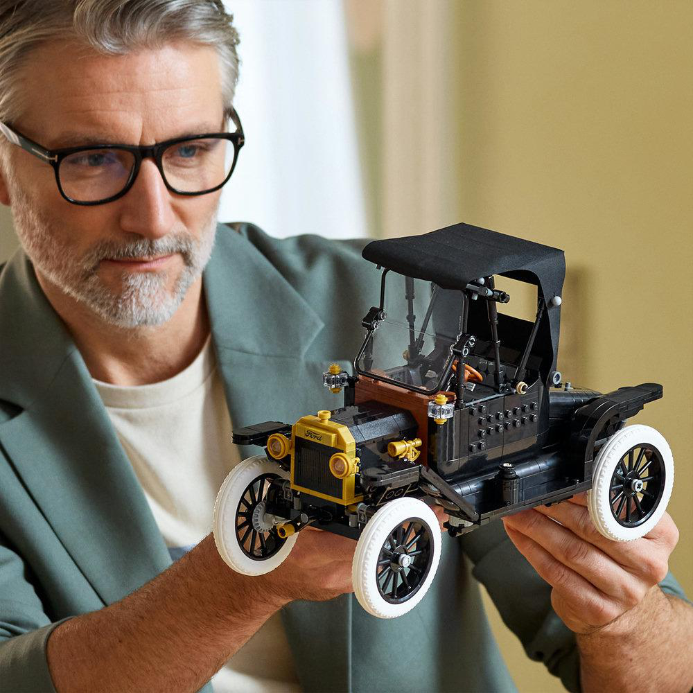 Mann hält ein schwarzes Ford Modell T Lego Auto mit weißen Reifen.
