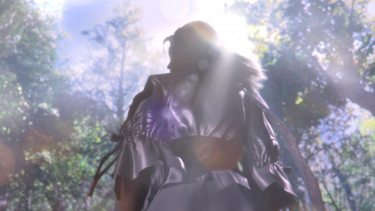 Rückansicht einer Frau in einem glänzenden Kleid im Wald, Sonnenlicht scheint durch Bäume.