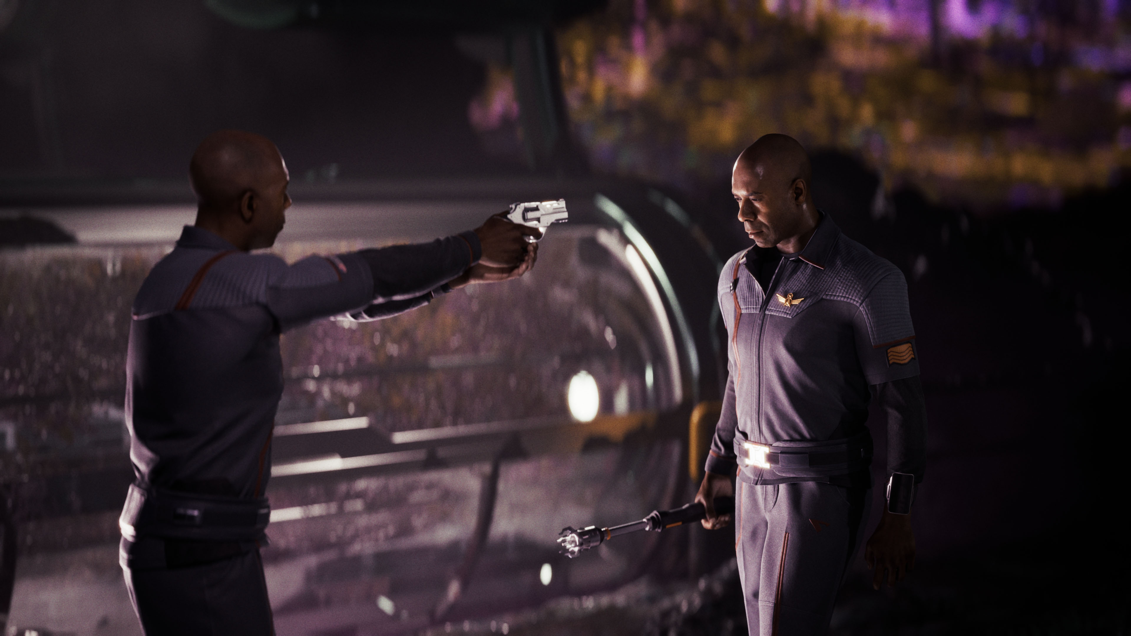 Mężczyzna w mundurze celuje pistoletem w innego mężczyznę trzymającego urządzenie.