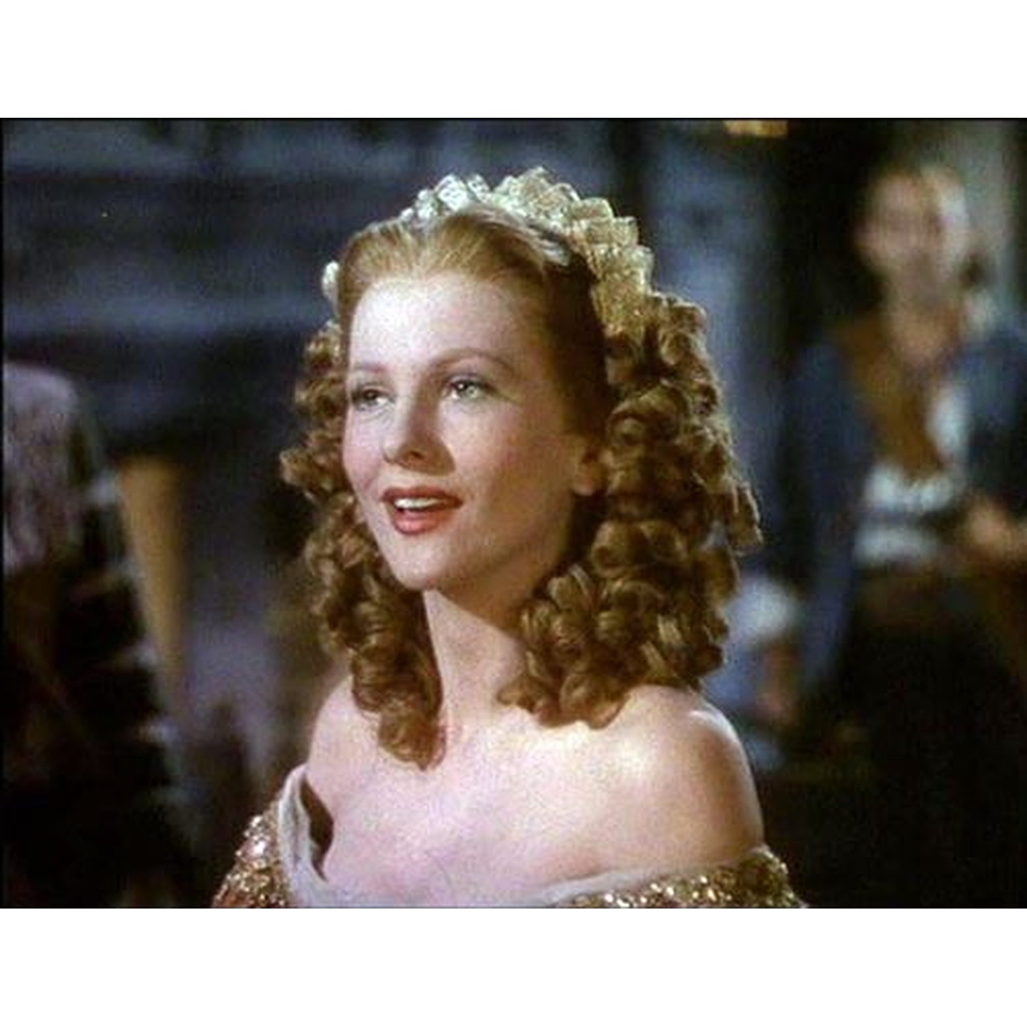 Een vrouw met rood haar en een tiara draagt een roze jurk.