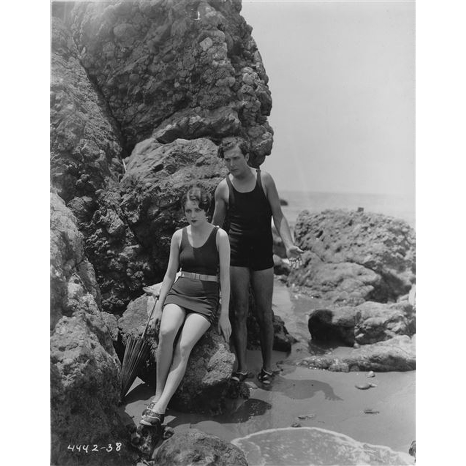 Homme et femme en maillot de bain sur une plage rocheuse.