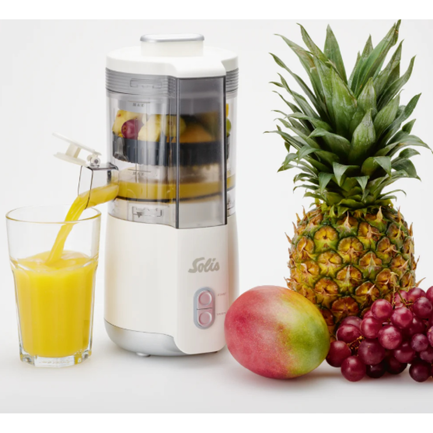Een sapcentrifuge perst sap in een glas, met mango, druiven en ananas ernaast.