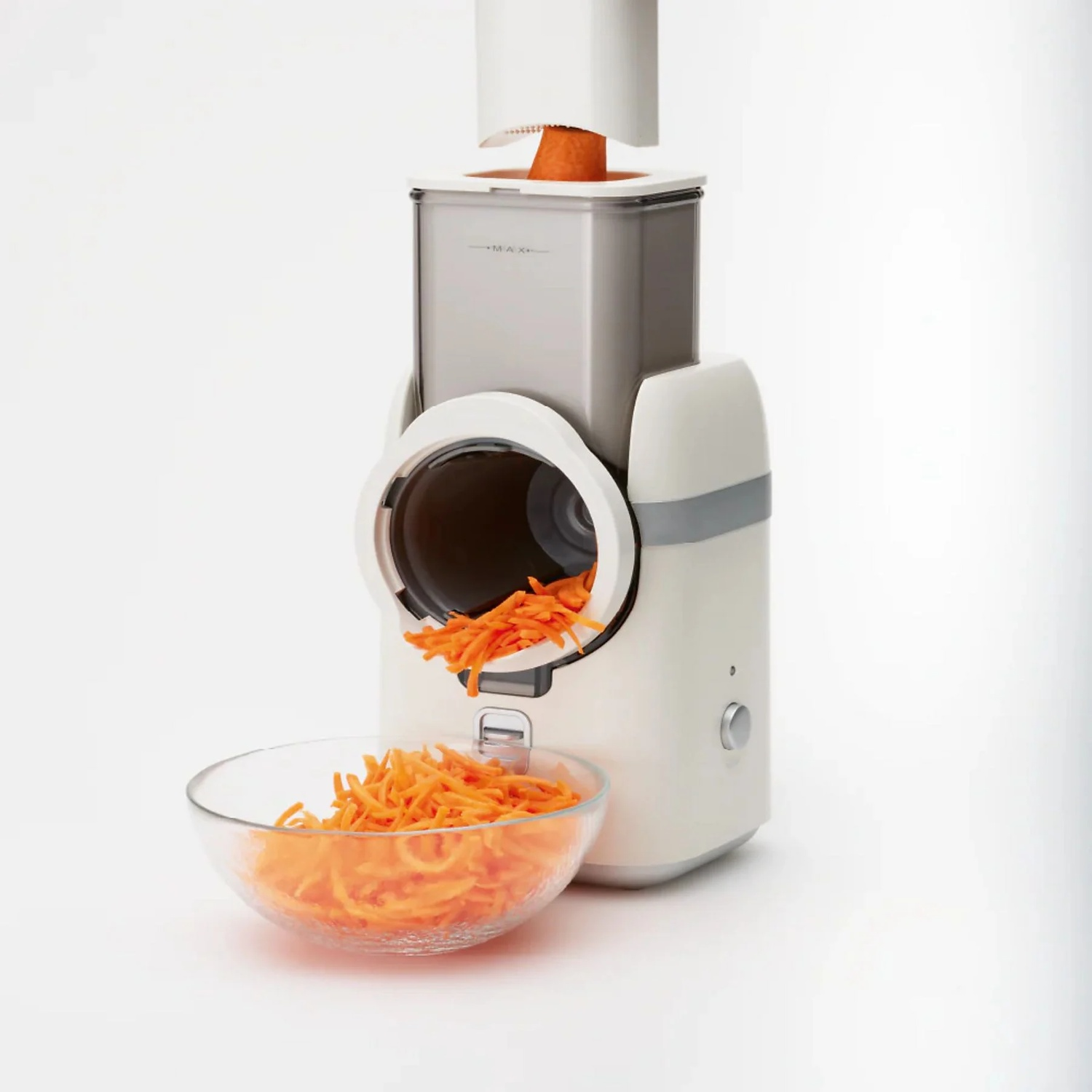 A carrot is being shredded into strips by an electric grater, falling into a bowl.
