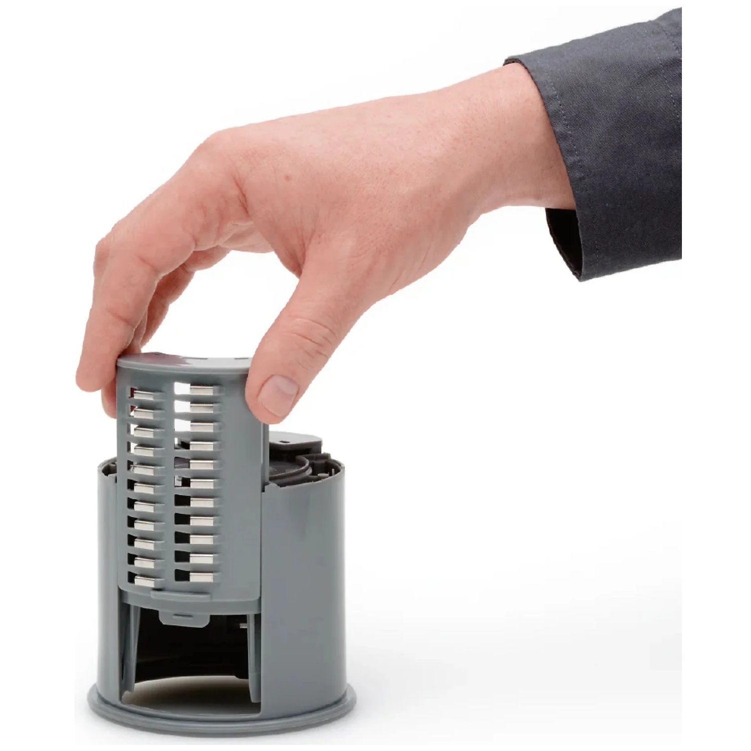 A hand holds a gray insert with slots and metal strips.