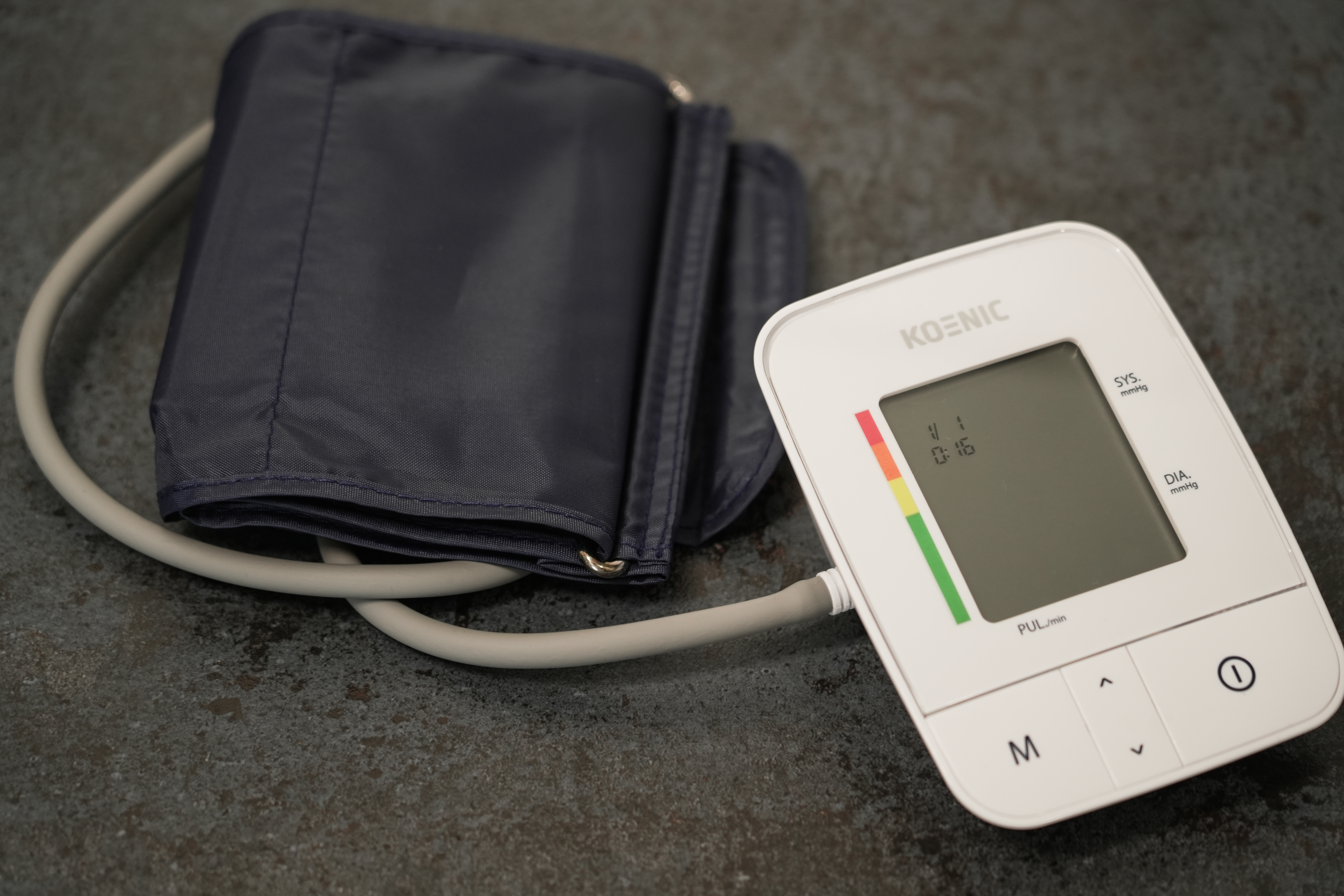 Biały ciśnieniomierz z mankietem na ciemnym tle.