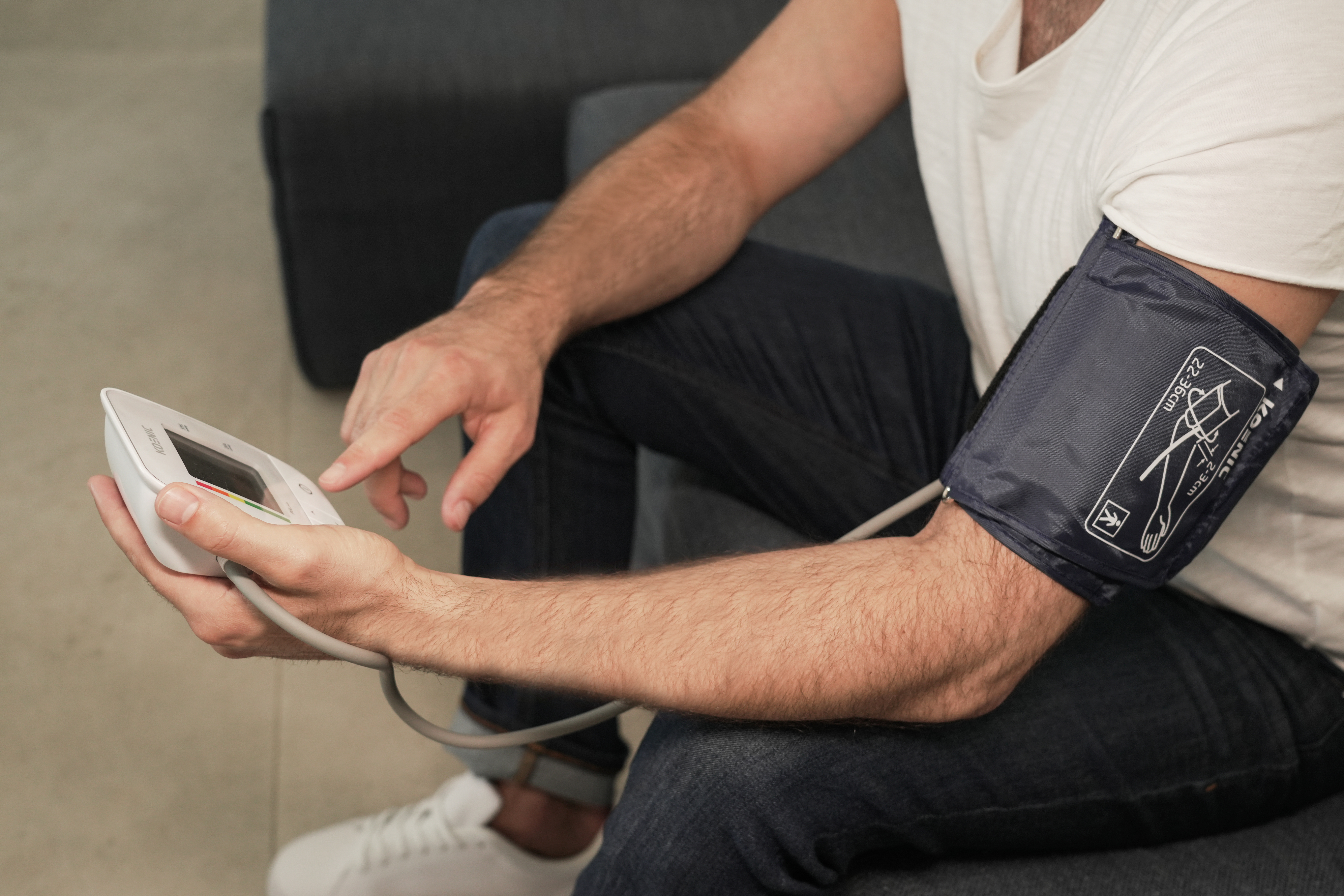 Mężczyzna mierzy ciśnienie krwi urządzeniem z mankietem na ramieniu.