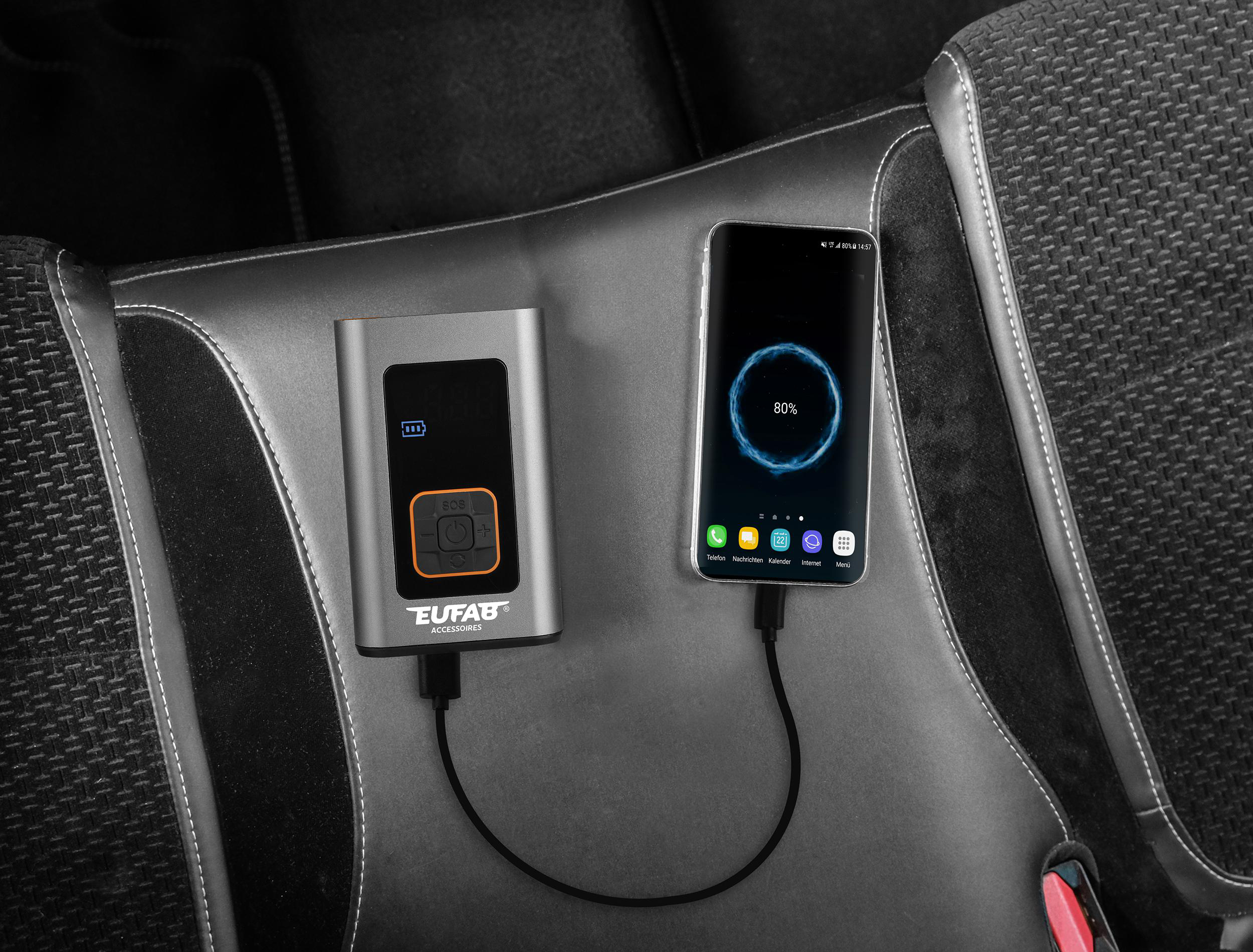 Grauer Akku und Smartphone laden nebeneinander auf einem Autositz.
