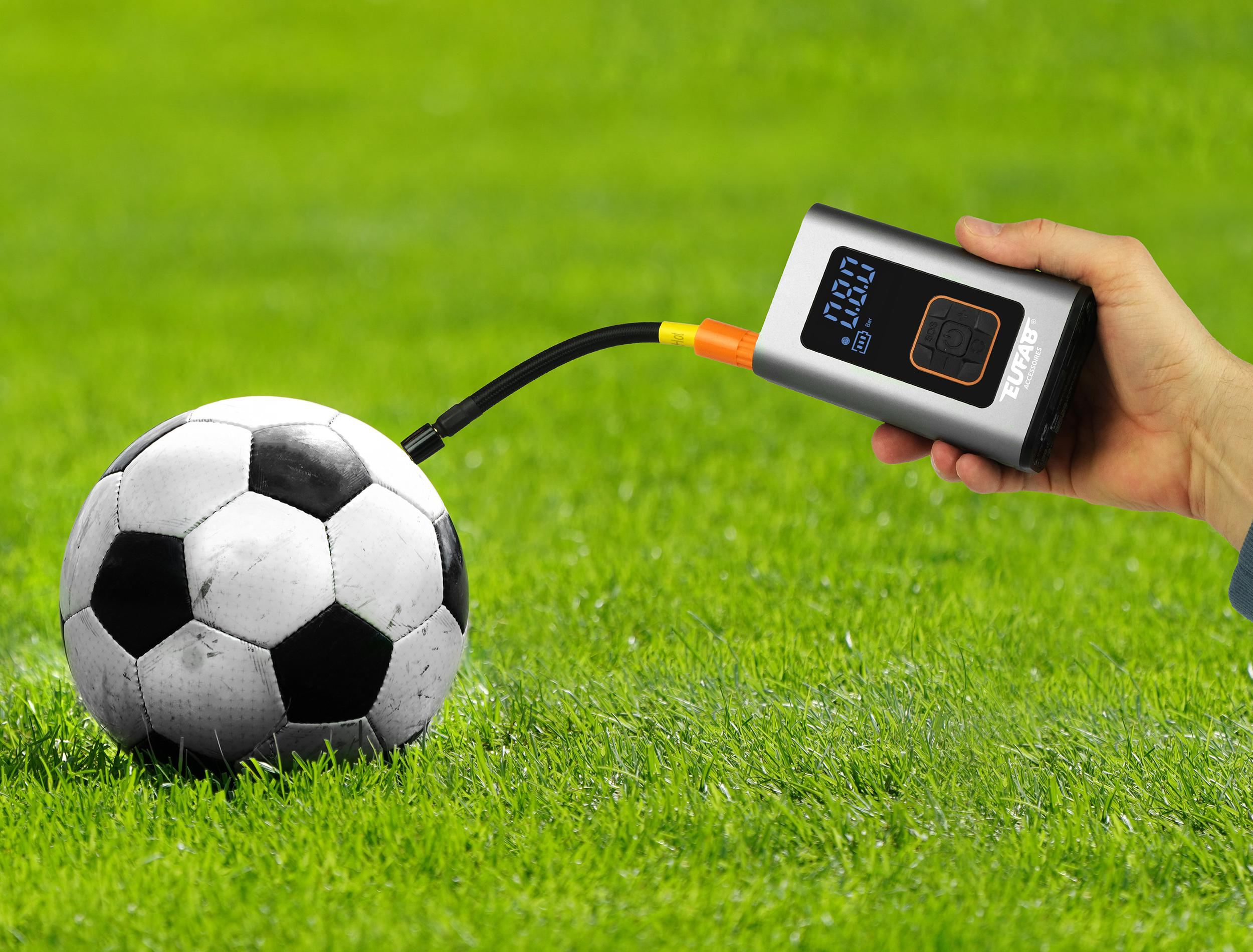 Ein Mann pumpt einen Fußball auf einem grünen Rasen mit einem digitalen Reifendruckprüfer auf.